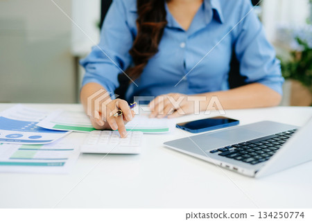Women counting coins on calculator taking from the piggy bank. hand holding pen working on calculator to calculate on desk about cost 134250774