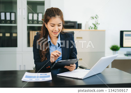 Asian woman with a smile standing holding notepad and tablet at the modern office. 134250917