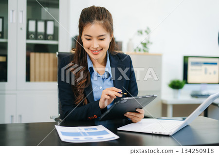 Asian woman with a smile standing holding notepad and tablet at the modern office. 134250918