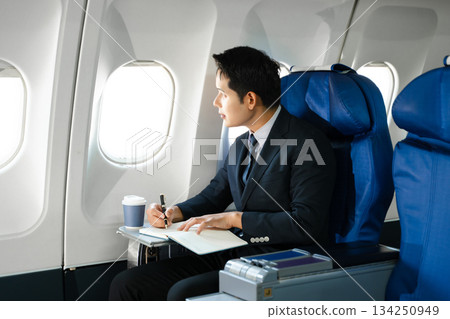 Confident businessman enjoying luxury air travel in first class, working on a tablet with a coffee, blending business, technology, and global connectivity. 134250949