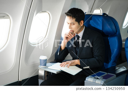Confident businessman enjoying luxury air travel in first class, working on a tablet with a coffee, blending business, technology, and global connectivity. 134250950