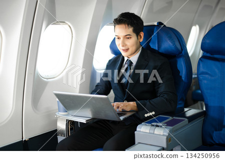 Confident businessman enjoying luxury air travel in first class, working on a tablet with a coffee, blending business, technology, and global connectivity. 134250956