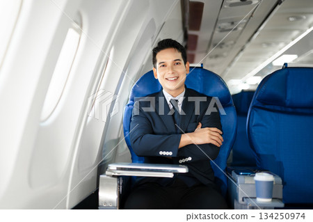 Smiling businessman in a suit giving a thumbs up while seated in first class, symbolizing success, confidence, and luxury air travel for business professionals. 134250974