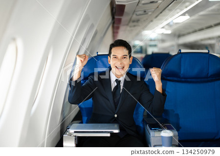Smiling businessman in a suit giving a thumbs up while seated in first class, symbolizing success, confidence, and luxury air travel for business professionals. 134250979