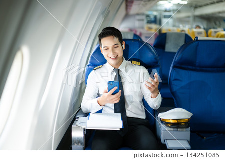 Confident airline pilot in uniform using wireless earbuds while reviewing documents, perfect for aviation, travel, and modern communication themes Confident airline pilot in uniform using wireless earbuds while reviewing documents, perfect for aviation, travel, and modern communication themes 134251085
