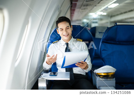 Confident airline pilot in uniform using wireless earbuds while reviewing documents, perfect for aviation, travel, and modern communication themes Confident airline pilot in uniform using wireless earbuds while reviewing documents, perfect for aviation, travel, and modern communication themes 134251086