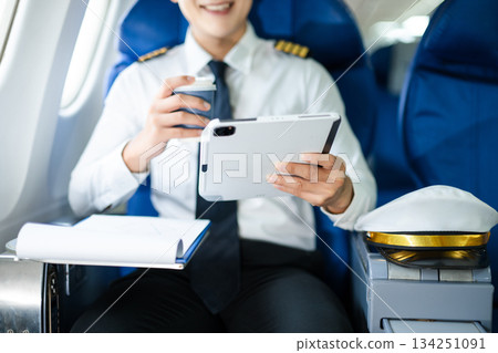 Confident pilot in uniform using smartphone in airplane cabin, ideal for aviation, communication, and travel lifestyle stock imagery. Confident pilot in uniform using smartphone in airplane cabin, ideal for aviation, communication, and travel lifestyle stock imagery. 134251091