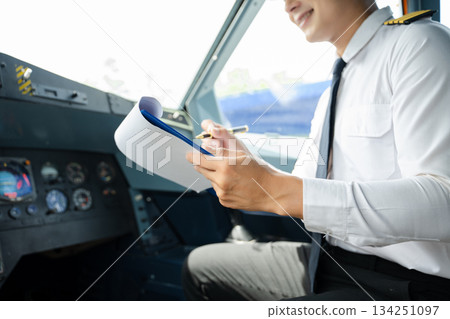 Professional airline pilot in uniform inspecting cockpit control panels during safety checks, ideal for aviation, travel, and airline safety themes. 134251097
