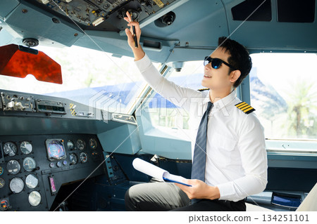 Professional airline pilot in uniform inspecting cockpit control panels during safety checks, ideal for aviation, travel, and airline safety themes. 134251101