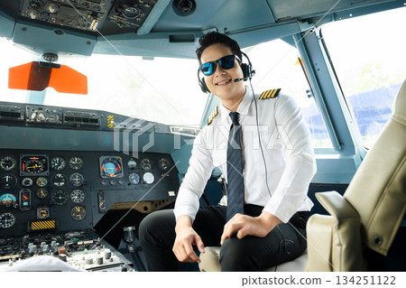 Airline pilot in uniform with headset giving thumbs up in airplane cockpit, ideal for aviation, travel, and professional aviation lifestyle stock imagery 134251122