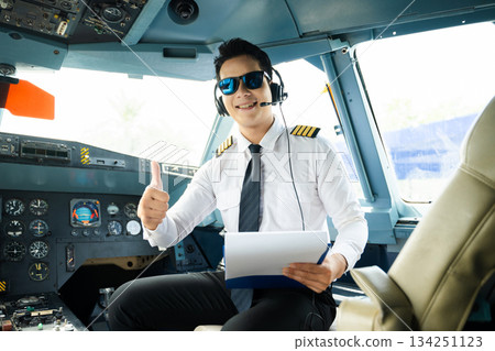 Airline pilot in uniform with headset giving thumbs up in airplane cockpit, ideal for aviation, travel, and professional aviation lifestyle stock imagery 134251123