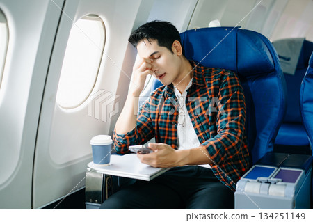 Travel stress, jet lag, or motion sickness. Young man with a headache or fatigue during a long flight. Tired passenger on a business trip. 134251149