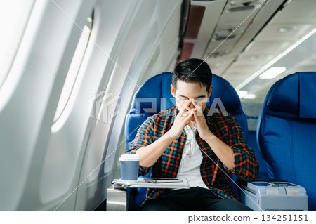 Travel stress, jet lag, or motion sickness. Young man with a headache or fatigue during a long flight. Tired passenger on a business trip. 134251151