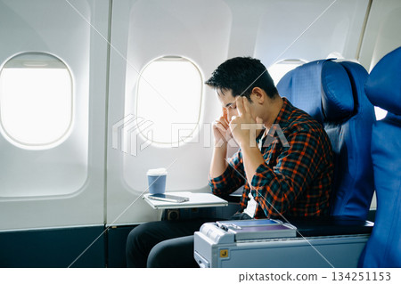 Travel stress, jet lag, or motion sickness. Young man with a headache or fatigue during a long flight. Tired passenger on a business trip. 134251153