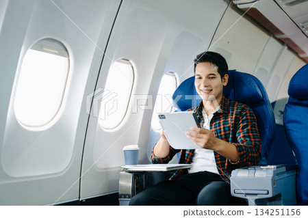 Happy traveler using modern tablet tech on a plane. Digital work, screen entertainment, or connecting with mobile internet on a business trip/journey. 134251156