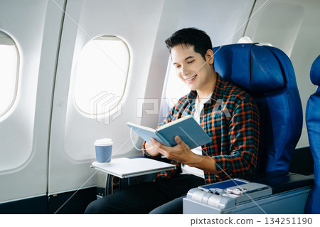 Happy young man traveling by plane. Business or leisure flight series showing phone talk, tech, reading, and stress. 134251190