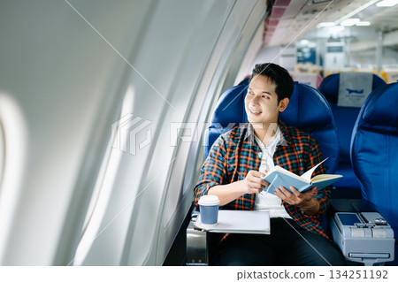 Happy young man traveling by plane. Business or leisure flight series showing phone talk, tech, reading, and stress. 134251192
