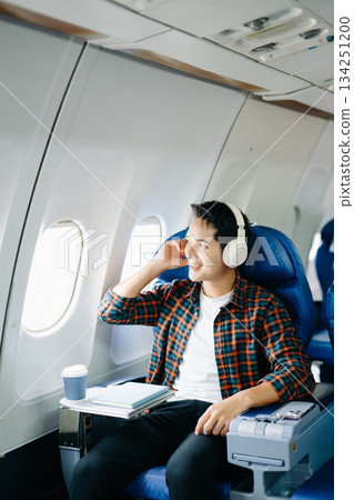 Happy man in a plane seat. Diverse travel series: work, talk, call, listen, read, stress, and joy on a long flight. Tech, mobile, and view are key parts of the trip. 134251200