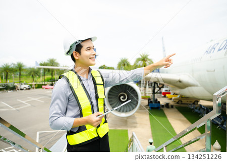 Ground crew engineer in safety vest and helmet pointing and holding documents during airplane inspection, perfect for aviation and flight safety themes Ground crew engineer in safety vest and helmet pointing and holding documents during airplane inspection, perfect for aviation and flight safety themes 134251226