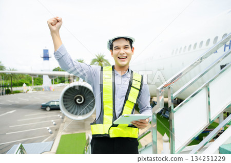 Ground crew engineer in safety vest and helmet giving thumbs up near airplane, ideal for aviation, safety, 134251229