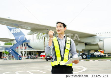 Ground crew engineer in safety vest and hard hat using walkie talkie while checking documents, perfect for aviation, maintenance, Ground crew engineer in safety vest and hard hat using walkie talkie while checking documents, perfect for aviation, maintenance, 134251231