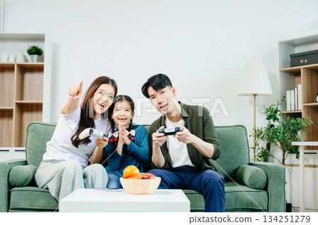 Happy Asian parents and child bonding, playing games, laughing, and enjoying social media together in cozy living room. Family time, love Happy Asian parents and child bonding, playing games, laughing, and enjoying social media together in cozy living room. Family time, love 134251279