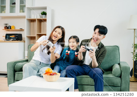 Happy Asian parents and child bonding, playing games, laughing, and enjoying social media together in cozy living room. Family time, love Happy Asian parents and child bonding, playing games, laughing, and enjoying social media together in cozy living room. Family time, love 134251280