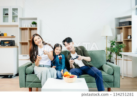 Happy Asian parents and child bonding, playing games, laughing, and enjoying social media together in cozy living room. Family time, love Happy Asian parents and child bonding, playing games, laughing, and enjoying social media together in cozy living room. Family time, love 134251281