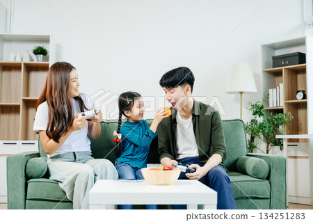 Happy Asian parents and child bonding, playing games, laughing, and enjoying social media together in cozy living room. Family time, love Happy Asian parents and child bonding, playing games, laughing, and enjoying social media together in cozy living room. Family time, love 134251283