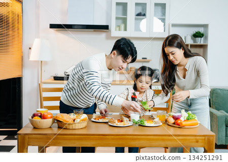 Happy Asian parents and daughter enjoying healthy breakfast together at home. Candid lifestyle family moment with food, love in kitchen. 134251291