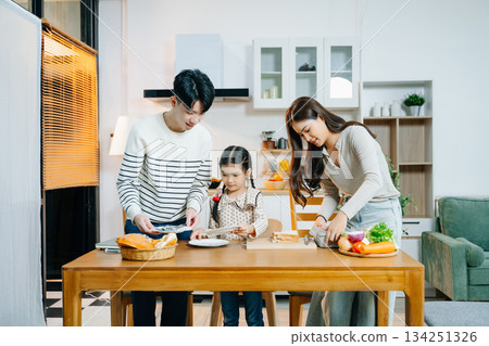 Asian family shares a happy morning, preparing and enjoying breakfast in a cozy kitchen. Parents and daughter bond over love 134251326