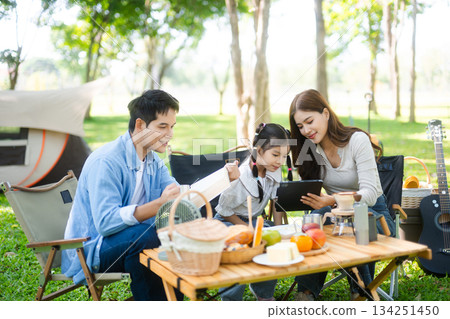 Joyful Asian family camping in a sunny garden, bonding over BBQ, tech, and laughter. Parents and daughter enjoy outdoor Joyful Asian family camping in a sunny garden, bonding over BBQ, tech, and laughter. Parents and daughter enjoy outdoor 134251450