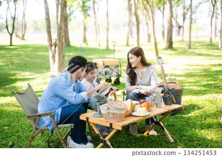 Joyful Asian family camping in a sunny garden, bonding over BBQ, tech, and laughter. Parents and daughter enjoy outdoor Joyful Asian family camping in a sunny garden, bonding over BBQ, tech, and laughter. Parents and daughter enjoy outdoor 134251453
