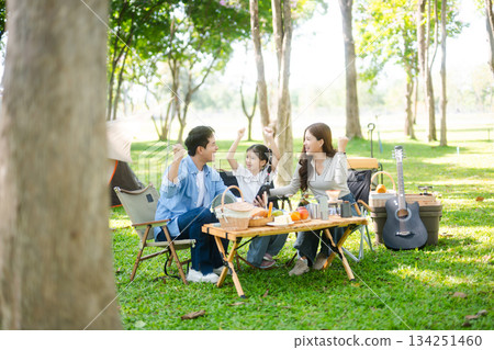 Joyful Asian family camping in a sunny garden, bonding over BBQ, tech, and laughter. Parents and daughter enjoy outdoor Joyful Asian family camping in a sunny garden, bonding over BBQ, tech, and laughter. Parents and daughter enjoy outdoor 134251460