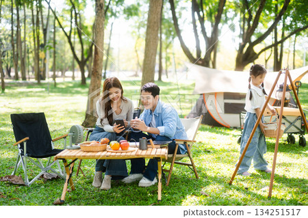 Asian couple enjoys a peaceful camping morning with coffee, breakfast, music, and devices in nature with love 134251517