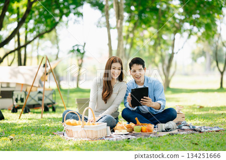 Asian couple enjoys a peaceful camping morning with coffee, breakfast, music, and devices in nature 134251666