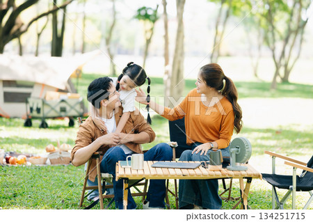 Joyful Asian family camping in a sunny garden, bonding over BBQ, tech, and laughter. Parents and daughter enjoy outdoor Joyful Asian family camping in a sunny garden, bonding over BBQ, tech, and laughter. Parents and daughter enjoy outdoor 134251715