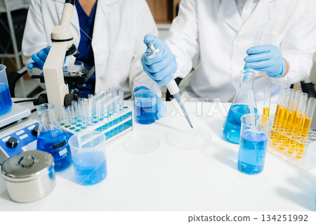 scientists in lab coats conducting research, handling glassware, and working with chemicals in a modern, high tech laboratory. 134251992