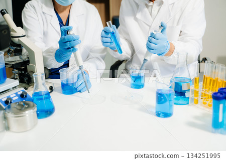 scientists in lab coats conducting research, handling glassware, and working with chemicals in a modern, high tech laboratory. 134251995