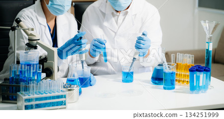 Two scientists in a high-tech lab analyzing biochemical samples, using micro pipettes Two scientists in a high-tech lab analyzing biochemical samples, using micro pipettes 134251999