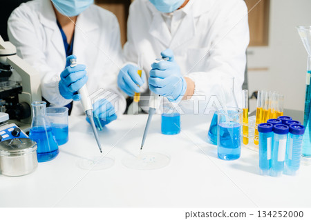 Two  scientists in a high-tech lab analyzing biochemical samples, using micro pipettes 134252000