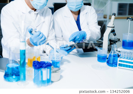 scientists in lab coats conducting research, handling glassware, and working with chemicals 134252006