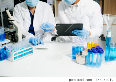 scientists in lab coats conducting research, handling glassware, and working with chemicals scientists in lab coats conducting research, handling glassware, and working with chemicals 134252019