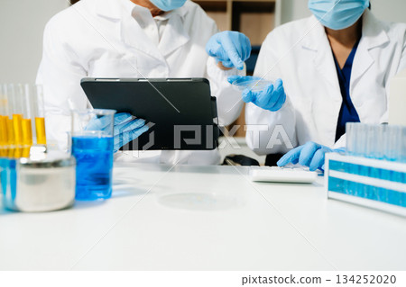 Scientists in a clean lab environment analyzing samples using test tubes and a tablet, showcasing modern biotech research, diagnostics, and medical innovation. 134252020
