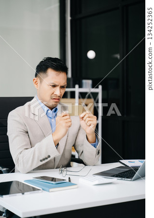 Frustrated young businessman working on a laptop computer sitting at his working place 134252365