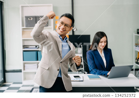 Young attractive Asian male office worker business suits smiling at camera in office Young attractive Asian male office worker business suits smiling at camera in office 134252372