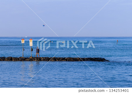 一名男子站在威基基防波堤上釣魚，眺望著大海和一架滑翔傘。 134253401