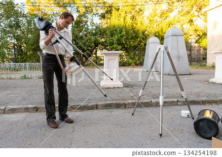 Man adjusts telescope mount tripod during evening setup outdoors 134254198