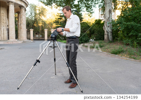 Man aligns telescope mount during outdoor evening setup 134254199
