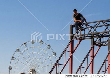 Freerunner sits atop structure with Ferris wheel behind 134254246